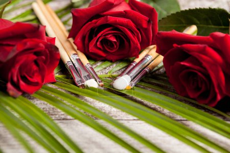 Foto de Pinceles de maquillaje junto a rosas sobre fondo de madera - Imagen libre de derechos