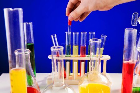 Téléchargez les photos : Person hand working in chemistry lab over blue background. Glassware and biology equipment - en image libre de droit