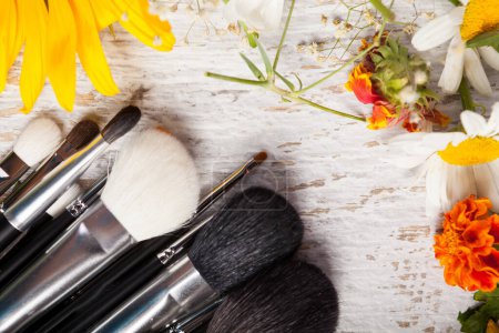 Téléchargez les photos : Make up brushes on a table next to wild flowers on wooden background - en image libre de droit