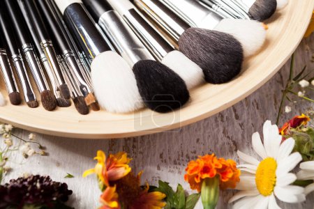 Téléchargez les photos : Professional Make up brushes on plate next to wild flowers on wooden background - en image libre de droit