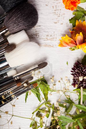Téléchargez les photos : Make up accessories next to wild flowers on wooden background - en image libre de droit