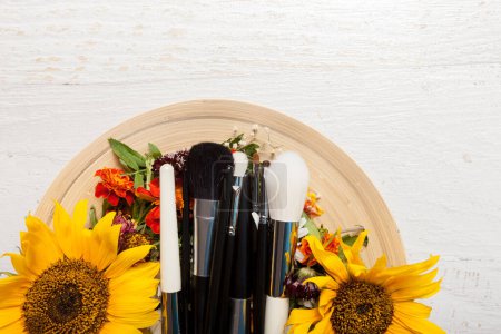 Téléchargez les photos : Brosses de maquillage sur plaque à côté de fleurs sauvages sur fond en bois - en image libre de droit