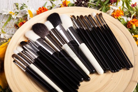 Téléchargez les photos : Brosses de maquillage sur une assiette à côté de fleurs sauvages sur fond en bois - en image libre de droit