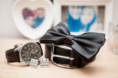 Foto de Botones de camisa, cinturón, reloj y arco en una mesa en el día de la boda - Imagen libre de derechos