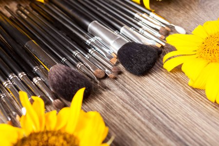 Téléchargez les photos : Make up brushes next to flowers on wooden background - en image libre de droit