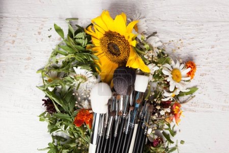 Téléchargez les photos : Make up brushes on a pile of wild flowers on wooden background - en image libre de droit