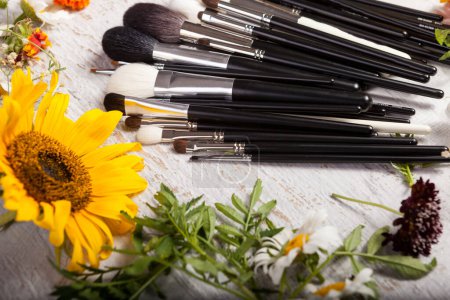 Téléchargez les photos : Brosses de maquillage sur une table à côté de fleurs sauvages sur fond en bois - en image libre de droit