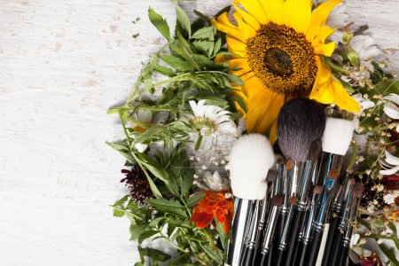 Téléchargez les photos : Make up brushes on a pile of wild flowers on wooden background - en image libre de droit