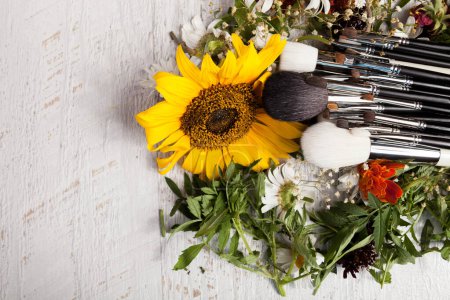 Téléchargez les photos : Brosses de maquillage sur un tas de fleurs sauvages sur fond de bois - en image libre de droit