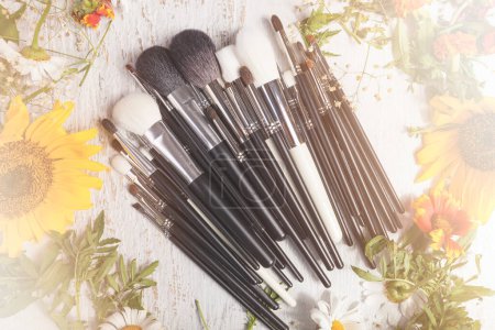 Téléchargez les photos : Make up brushes on wooden background next to wild flowers. Professional cosmetics - en image libre de droit