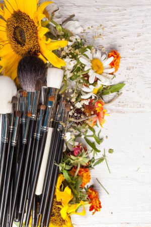 Photo for Make up brushes on a pile of wild flowers on wooden background - Royalty Free Image