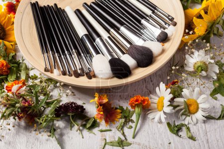 Téléchargez les photos : Brosses de maquillage professionnel sur plaque à côté de fleurs sauvages sur fond en bois - en image libre de droit