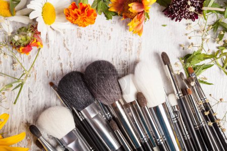 Téléchargez les photos : Make up brushes on wooden background next to wild flowers. Professional cosmetics - en image libre de droit