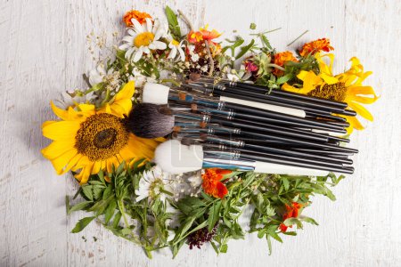 Téléchargez les photos : Brosses de maquillage sur un tas de fleurs sauvages sur fond de bois - en image libre de droit