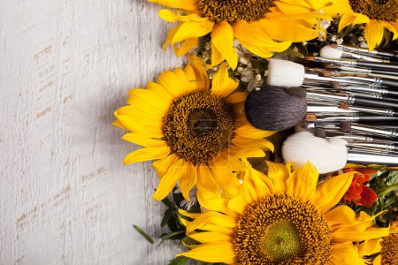 Téléchargez les photos : Make up brushes next to beautiful wild flowers on wooden background - en image libre de droit