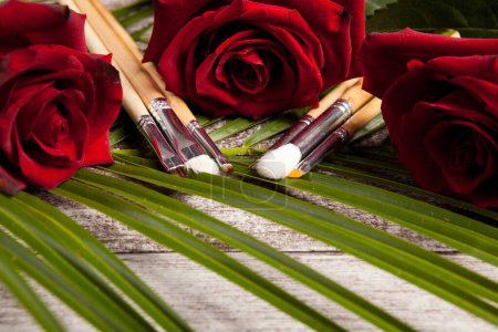 Photo for Makeup brushes next to roses on wooden background - Royalty Free Image
