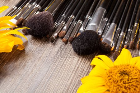 Foto de Make up brushes next to flowers on wooden background - Imagen libre de derechos