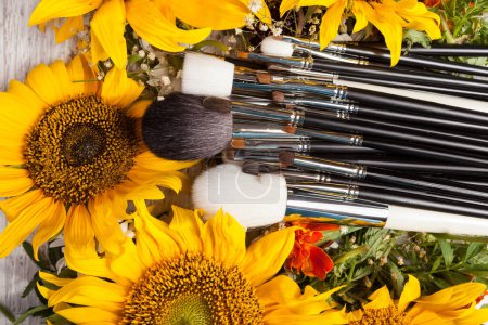 Téléchargez les photos : Brosses de maquillage à côté de belles fleurs sauvages sur fond en bois - en image libre de droit