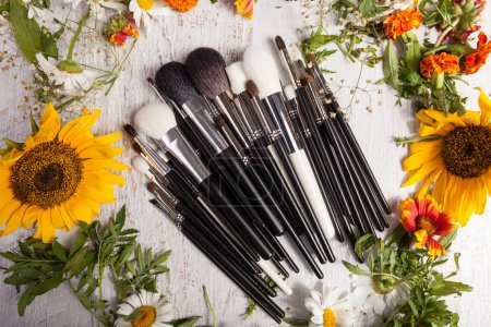 Photo for Make up brushes on wooden background next to wild flowers. Professional cosmetics - Royalty Free Image