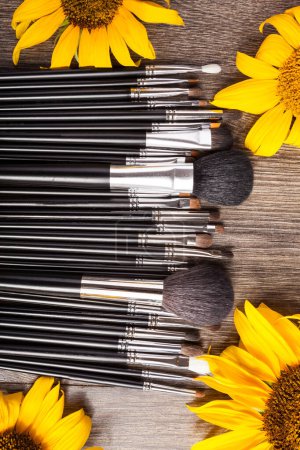 Foto de Professional Make up brushes next to beautiful wild flowers on wooden background - Imagen libre de derechos