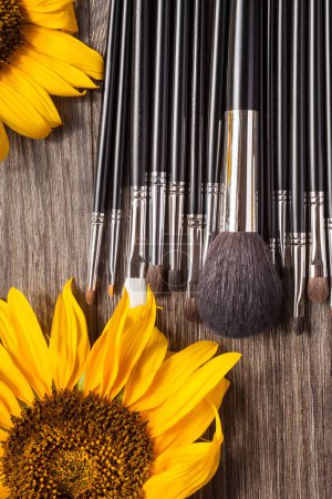 Téléchargez les photos : Professional Make up brushes next to beautiful wild flowers on wooden background - en image libre de droit