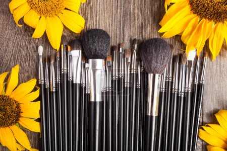 Photo for Professional Make up brushes next to beautiful wild flowers on wooden background - Royalty Free Image
