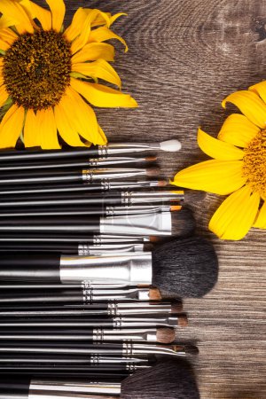 Téléchargez les photos : Brosses de maquillage professionnel à côté de belles fleurs sauvages sur fond en bois - en image libre de droit