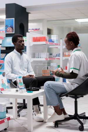 Photo for Pharmacist consultation, drugstore seller advising medicaments, holding pills package. African american man and medic talking, chemist and client communication, all black team - Royalty Free Image