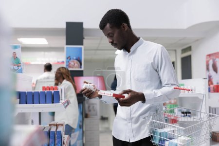 Photo for African american man checking food supplements in drugstore shelf, reading instruction on tablets package. Client choosing vitamins, buying prescription medications, side view - Royalty Free Image