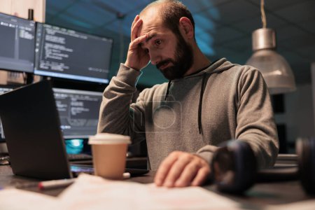 Photo for Stressed overworked developer programming html code on laptop and multiple monitors, working under stress after hours. Male app programmer feeling frustrated and tired coding data script. - Royalty Free Image