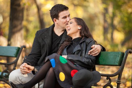 Foto de Feliz pareja enamorada sentada en un banco en el parque de otoño - Imagen libre de derechos