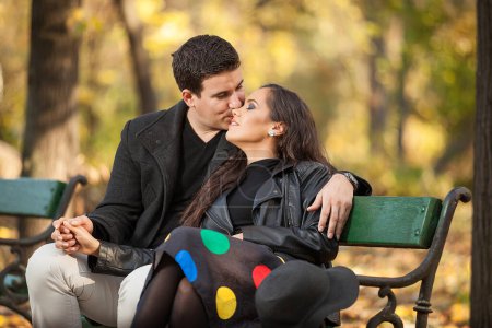 Foto de Feliz pareja enamorada sentada en un banco en el parque de otoño - Imagen libre de derechos