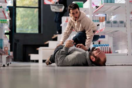 Téléchargez les photos : Woman running to man having seizure in medical retail store. Pharmacy scared customer rushing to give first aid to person lying on floor suffering from epileptic attack and foaming at mouth - en image libre de droit
