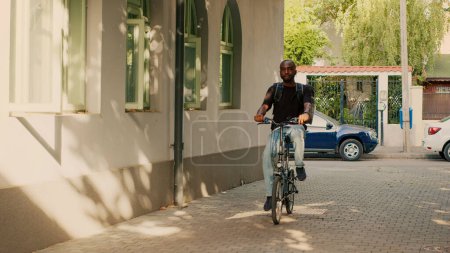 Photo for Food delivery service employee with backpack riding bike, delivering fastfood takeaway order at front door. Male courier using bicycle to give restaurant food and lunch meal. Paperbag package. - Royalty Free Image