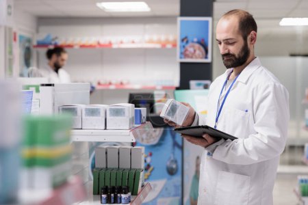 Photo for Drugstore employee looking at drugs packages typing medicaments name on tablet computer during inventory in pharmacy. Pharmacist is an expert in pharmaceuticals and is able to provide guidance - Royalty Free Image