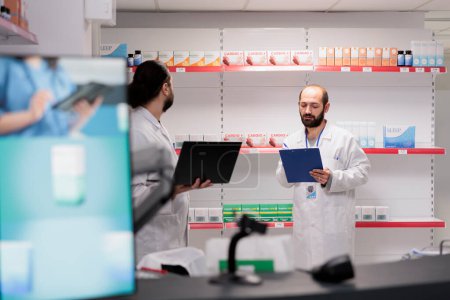 Foto de Drugstore workers working at pharmaceutical pills inventory checking drugs packages writing medical info on papers. Pharmacy is a vital resource for patients in need of medication and treatment. - Imagen libre de derechos