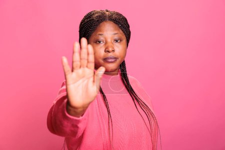 Photo for Irritated model doing stop symbol with palm expressing refusal and denial posing in studio with pink background. Young adult denying and disapproving with idea, raising hand decline suggestion. - Royalty Free Image