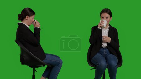 Téléchargez les photos : Close up of company worker serving coffee mug on camera, drinking caffeine refreshment and sitting on chair in studio. Businesswoman enjoying beverage and drink wearing formal office suit. - en image libre de droit