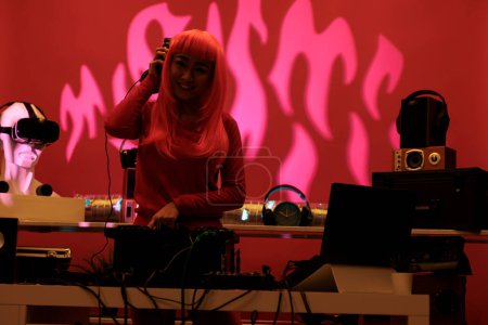 Téléchargez les photos : Femme asiatique aux cheveux roses mélangeant de la musique techno sur des platines tournantes tout en jouant des sons de mix en studio avec fond rose. Interprète s'amuser tout en interprétant une chanson électronique, profiter de la vie nocturne - en image libre de droit