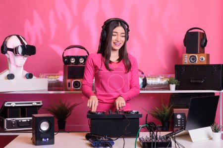 Téléchargez les photos : Artiste asiatique exécutant le son électronique à la console de mixage professionnel en studio, appréciant mélanger le son techno pendant le concert. Interprète joyeux jouant des sons stéréo avec électronique et microphone - en image libre de droit