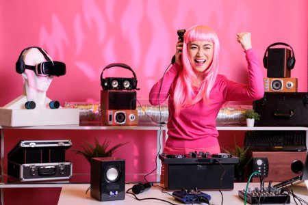 Téléchargez les photos : Asiatique dj avec les cheveux roses mélangeant la musique techno avec eletronic avoir du plaisir dans le club pendant la nuit, en interprétant la chanson en utilisant des platines tournantes professionnelles. Artiste célébrant l'album avec les fans en studio - en image libre de droit