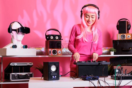 Artist with headphones playing electronic song at professional turntables, performing techno music in front of fans. Musician with pink hair doing performance at nightclub with audio equipment
