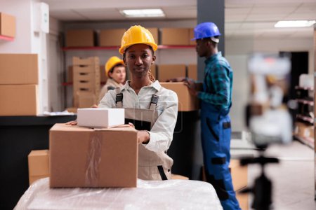 Photo for African american warehouse operator managing parcels receiving portrait. Industrial storehouse manager preparing freight cardboard boxes for export transportation and looking at camera - Royalty Free Image
