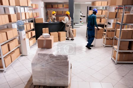 Photo for Post office storage workers managing parcels delivery, carrying and packing cardboard boxes. Logistics department employees preparing freight for distribution in industrial warehouse - Royalty Free Image