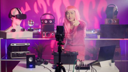 Téléchargez les photos : Artist performing song in studio recording mixing process with phone camera, playing eletronic song using professional turntables. Musician with pink hair having fun during performance - en image libre de droit