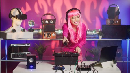Photo for Smiling artist standing at dj table enjoying mixing stereo sounds with electronics, having fun in club at night. Asian performer enjoying to perform music using professional audio equipment - Royalty Free Image