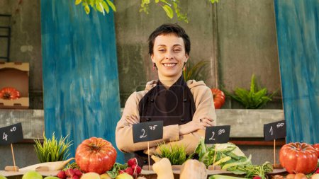 Foto de Retrato de una mujer agricultora vendiendo productos saludables en el mercado local, mostrando frutas y verduras ecológicas de temporada en el mercado de agricultores. Vendedor joven que se prepara para vender alimentos biológicos. - Imagen libre de derechos