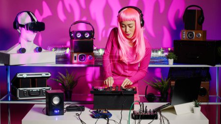 Smiling performer dancing and mixing techno sound with electronic using professional turntables, having fun during concert in nightclub. Performer standing over pink background in studio