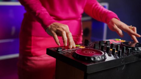 Artist standing at dj table mixing sound using mixer console, performing new album during night party in club. Musician enjoying playing music using professional audio equipment. Close up
