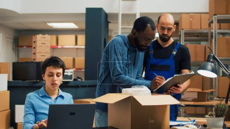 Foto de Entrepreneurs team preparing shipment order with products from warehouse racks, working on delivery logistics with laptop. Diverse people planning business development, supply chain. - Imagen libre de derechos